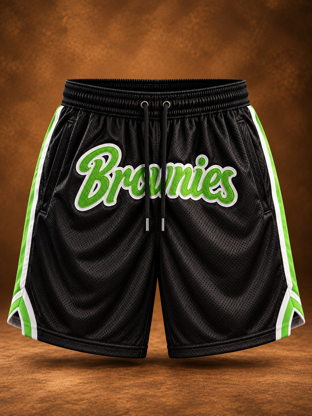 Black mesh basketball shorts with green and white side stripes and a large green 'Brownies' script across the front, shown against a brown textured background.